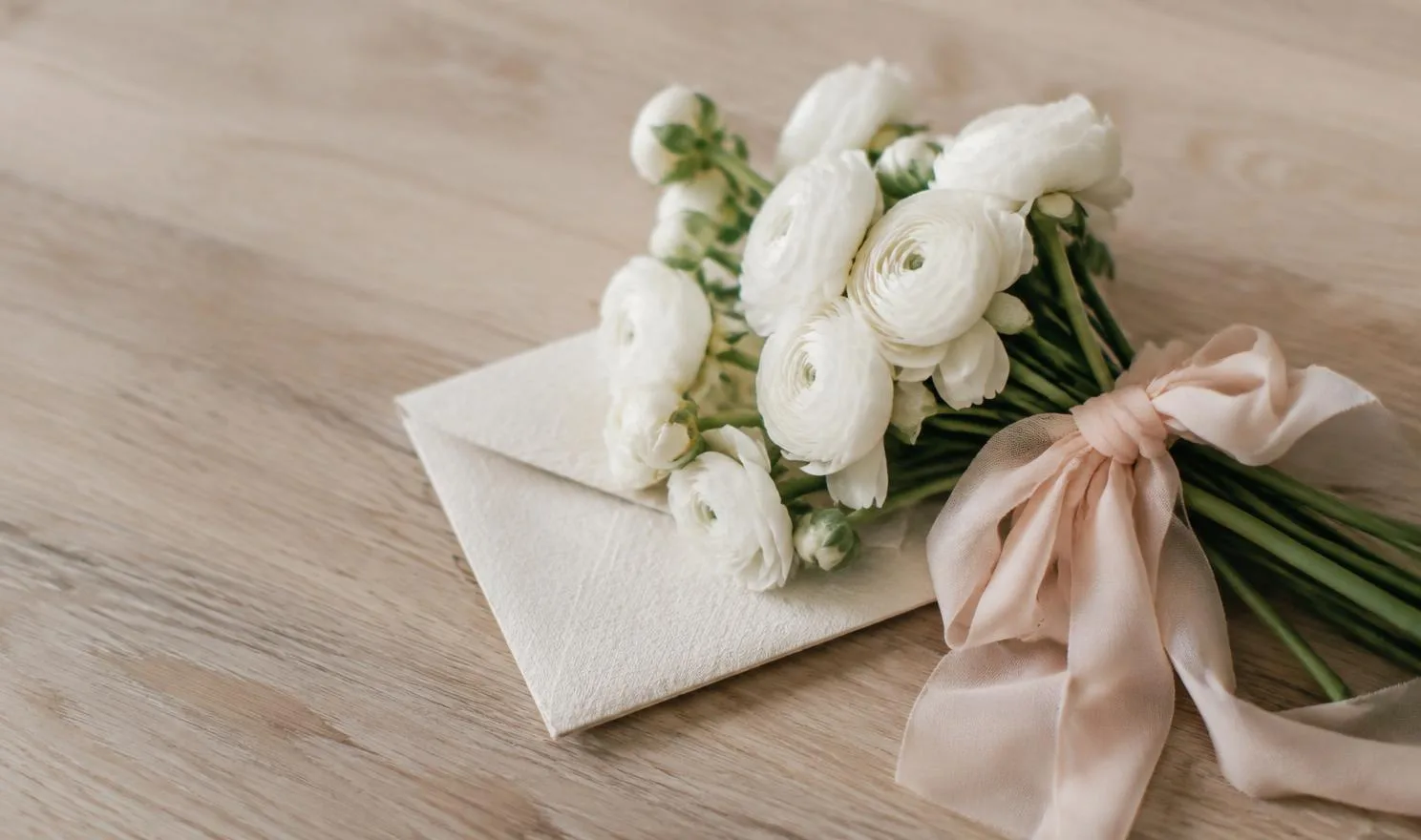 White ranunculus tied with blush silk ribbon on an ivory linen envelope