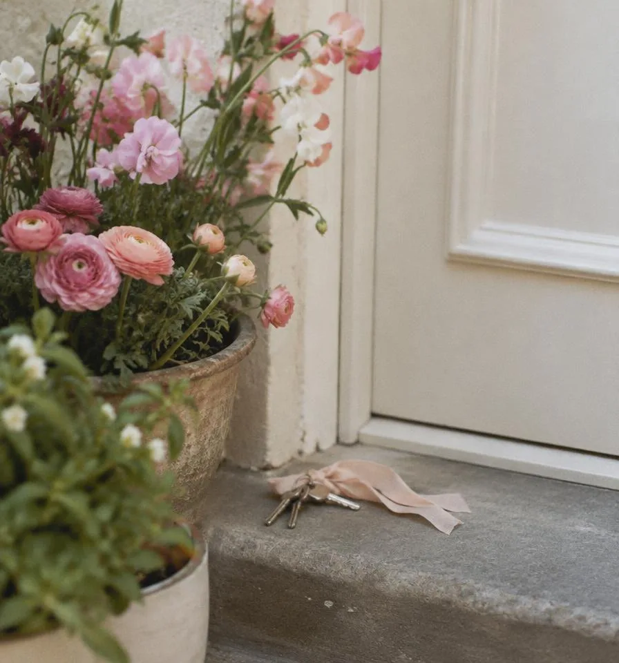 House keys with a ribbon on a doorstep beside potted flowers